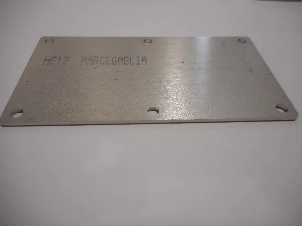 Metallplatte mit vorgebohrten Löchern, beschriftet mit "HE12 MARCEGAGLIA". Teil eines Heizsystems, möglicherweise zur Verwendung in Remeha-Produkten.